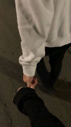 two people holding hands walking down the street at night with one person in white shirt and black pants