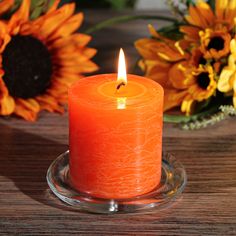 an orange candle sitting on top of a glass plate next to flowers and sunflowers