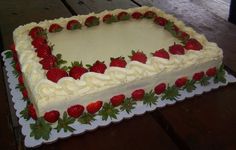 a large cake with strawberries on it is sitting on a wooden table and has white frosting