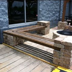 a wooden bench sitting on top of a sidewalk next to a fire pit in front of a building