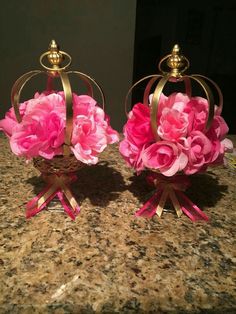 two pink flowers are sitting on top of each other in baskets with gold trimmings