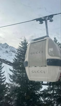 a gondola with the word gucci on it hanging from a wire in front of snow covered mountains