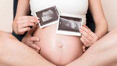 a pregnant woman is holding two photos in her belly while sitting on the floor with her stomach exposed