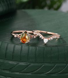 two gold rings with an orange stone and white diamonds on top of a green surface