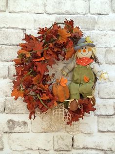 a scarecrow doll sitting in front of a wreath with autumn leaves on the ground