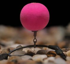 a pink ball sitting on top of a hook in the middle of some rocks and gravel