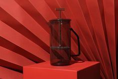 a glass coffee pot sitting on top of a red box next to a red wall