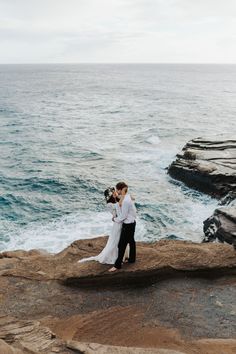 a bride and groom standing on rocks by the ocean