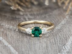 an emerald and diamond three stone ring sitting on top of a piece of fabric,