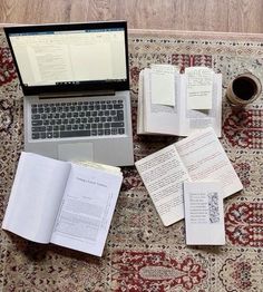 an open laptop computer sitting on top of a rug covered in books and papers next to a cup of coffee