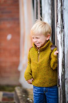 a little boy that is standing up against a wall with his hand on the door