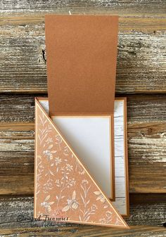 an orange and white card in a box on wooden planks with a brown envelope