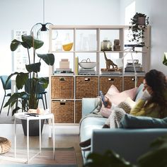 a woman sitting on a couch reading a book next to a plant in a living room