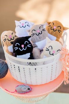 a basket filled with stuffed animals sitting on top of a pink table next to a ball of yarn