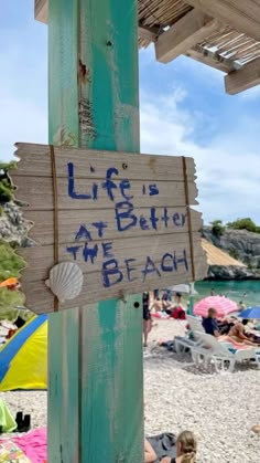 a wooden sign that says life is better at the beach with people in the background