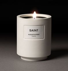 a white candle that is sitting on a table next to a black background with the word saint in it