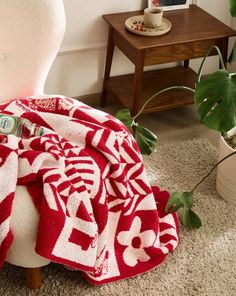 a red and white blanket sitting on top of a chair next to a potted plant