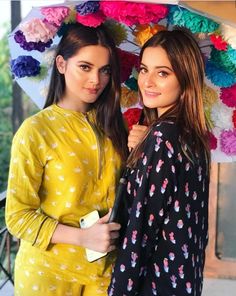 two young women standing under an umbrella with flowers on the top and one woman holding an umbrella over her head