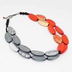 Make a bold statement with the Adira necklace. The double strand design is adorned with vibrant orange and gray beads, accented with gold and silver painted touches that add luxury to this piece. The adjustable chain allows for a perfect fit, while the oval wood beads add drama and fashion appeal. Elevate any outfit with this exquisite piece. Adjustable length: 20" - 22" Bead Dimensions: 1" x 1 1/2"  Care Instructions: Remove jewelry when applying perfumes, creams, washing hands, etc. Do not store in direct sunlight. To restore color and shine, apply a drop of oil with a soft cloth. Luxury Statement Multi-strand Beaded Necklace, Necklace Orange, Gray Necklace, Washing Hands, Grey Beads, Necklace Elegant, Color Necklace, Elegant Necklace, Elegant Necklaces