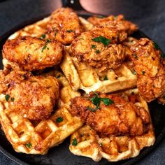 fried chicken and waffles are piled on top of each other in a black plate