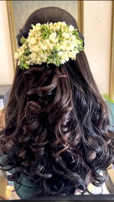 the back of a woman's head with flowers in her hair and long curly hair