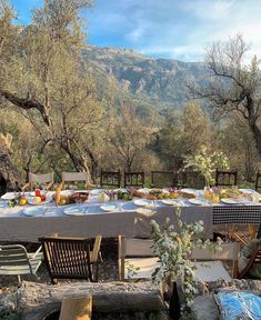 an outdoor table set up with plates and glasses on it in the middle of some trees