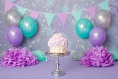 there is a cake on the table with purple and blue decorations around it, as well as balloons