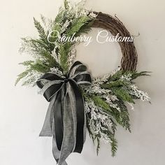 a wreath hanging on the wall with black and white ribbon around it, decorated with greenery