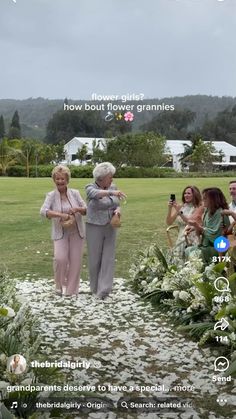 two women standing in the middle of a field with flowers on it and people taking pictures