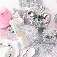 disco balls, silver cups and spoons on a table with pink tissue pom - poms