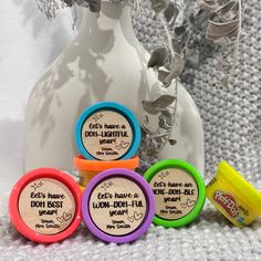 four different colored jars with labels on them sitting next to a white vase filled with flowers