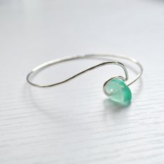 This sterling silver ocean wave bracelet is accented with cultured sea glass in beautiful hues of green. Bracelet is made with 14g sterling silver wire and hammered for a textured look. Each piece is hand formed, which adds to its unique and original quality, so please allow for slight variations. **Please also allow for variations in size and shape of sea glass** Hand Wrapped Green Sterling Silver Jewelry, Wire Wrapped Silver Jewelry With Recycled Glass, Wire Wrapped Silver Recycled Glass Jewelry, Turquoise Bangle For Beach, Beach Bangle Bracelets In Metal, Playful Beach Bangle Jewelry, Handmade Recycled Glass Bracelet, Handmade Sea Glass Bracelet As Gift, Handmade Sea Glass Bracelet For Gift