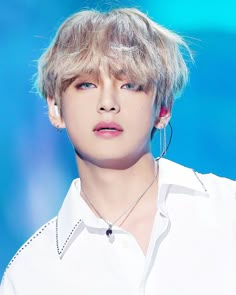 a young man with blonde hair wearing a white shirt and silver hoop earrings on his neck