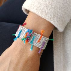 a person wearing a bracelet with colorful beads and tassels on their wrist,