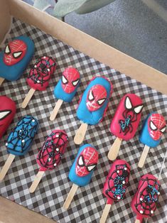 spiderman lollipops are sitting in a box on a checkered tablecloth