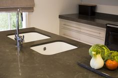 a kitchen counter top with two sinks and vegetables on the cutting board next to it