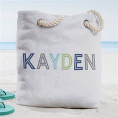 a white bag with the word kayden written on it next to blue flip flops