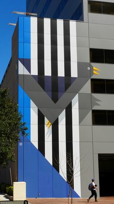 a man walking past a tall building with blue and white stripes on it's side