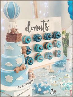 a blue and white dessert table with donuts on the top, hot air balloons in the background