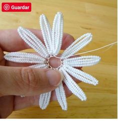 a hand holding a white beaded flower on a string