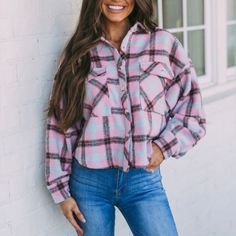 a woman leaning against a wall wearing a pink and black plaid shirt with long sleeves