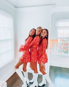 three girls in red dresses and white boots posing for the camera with their arms around each other