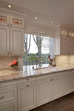 a large kitchen with marble counter tops and white cabinetry, along with an open window