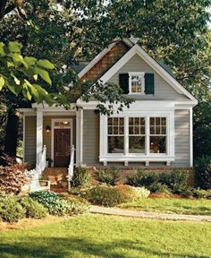 a small gray house with white trim and green shutters on the front door is shown