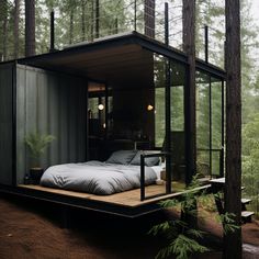 a bed in the middle of a forest with glass walls and windows on each side