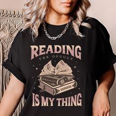 ♥ HAND-DRAWN ART: "Reading *The Occult* Is My Thing"  This whimsical, Booktrovert-inspired grimoire t-shirt is the perfect gift for feral aunts, witches, and mystical souls! Rock this super soft tee in one of 4 Comfort Color® favorites to match your soft goth, witchcore aesthetic. The design is on the front and features a one-of-a-kind, hand-drawn design you won't find anywhere else!  ♥ CREWNECK VERSION: Coming soon! ♥ TOTE BAG VERSION: Coming soon! ♥ MAD LOON SHOP: https://www.etsy.com/shop/madloonstudios ♦ ITEM QUICK FACTS » Direct To Garment (DTG) printing for a long-lasting, soft design » 100% cotton, unisex, short-sleeve t-shirt » Wash with cold water, iron on cool, do not dry clean ♦ UNISEX SIZING SM - 2XL » For an oversize fit, purchase 2 sizes larger » Larger sizes available upon r Black Literary T-shirt With Letter Print, Black Literary Crew Neck T-shirt, Black Bookish T-shirt With Screen Print, Black Literary Top With Graphic Print, Banned Books Tshirt, Witchcore Aesthetic, Book Tshirts, Banned Books, Top Books