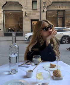 a woman sitting at a table with food and drinks in front of her on the street