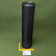 a roll of black woven fabric sitting on top of a green floor next to a measuring tape