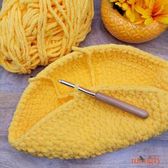 two balls of yarn and a crochet hook on a wooden surface with flowers in the background