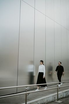 two people are walking down the stairs in front of a glass wall and metal railing